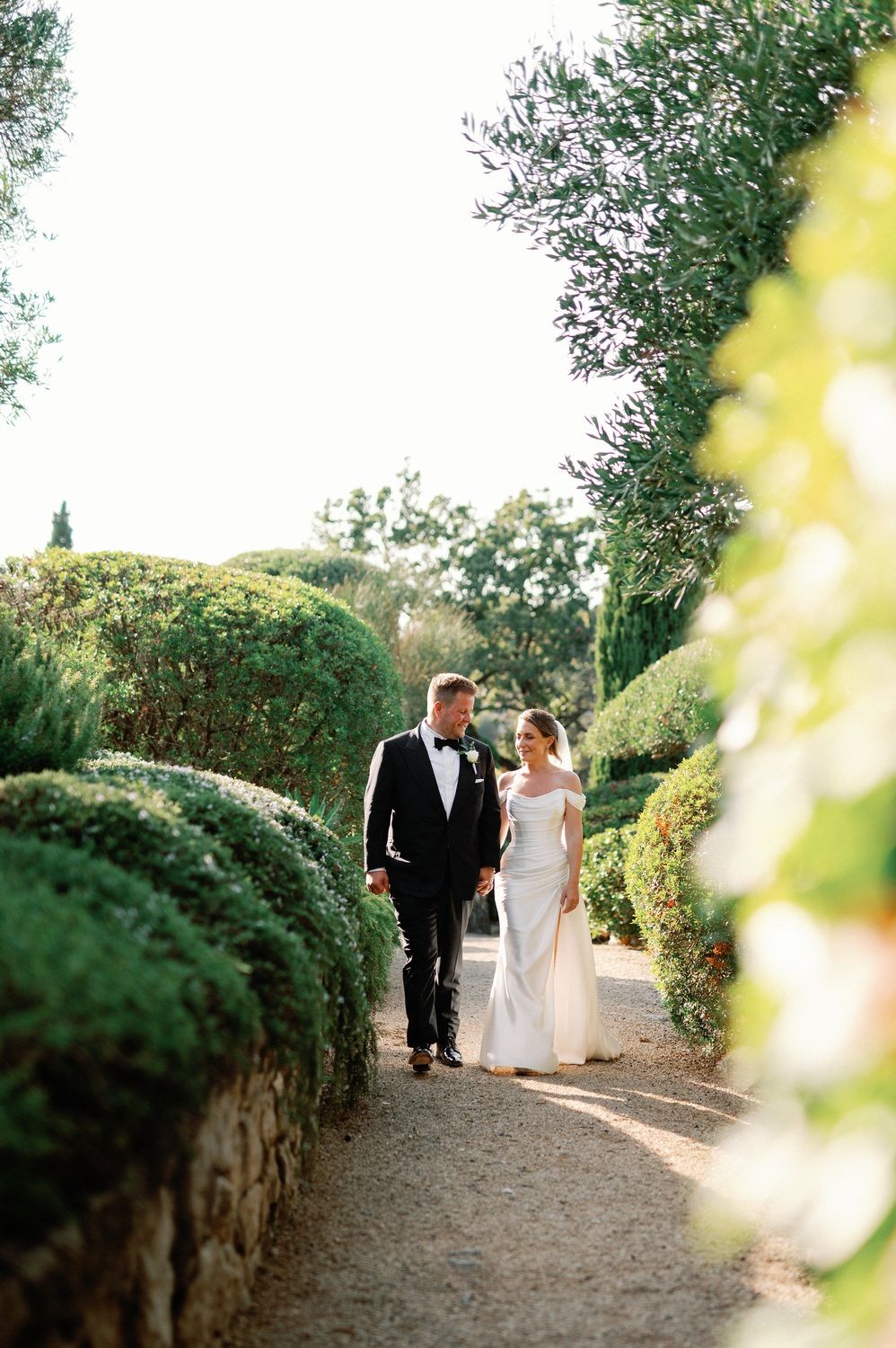 Wedding couple strolling together on a manicured garden pathway.