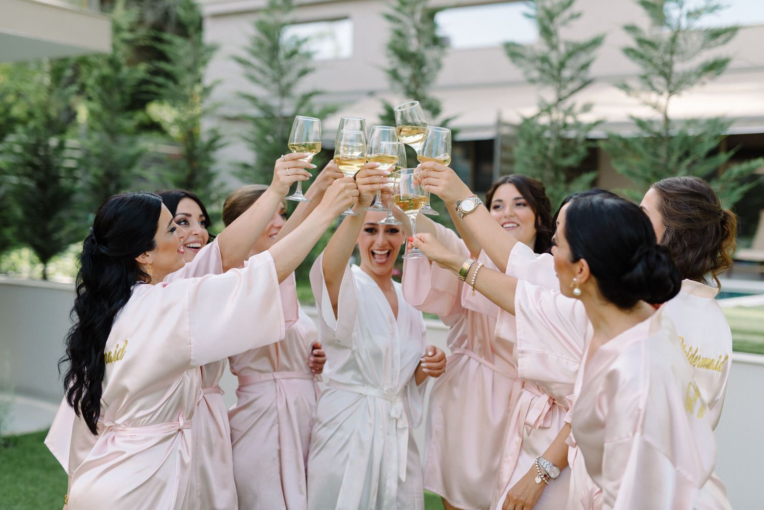 Bridesmaids in pink robes circle around to toast with champagne glasses.