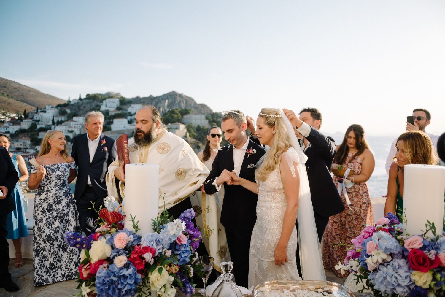 Wedding guests gather on a scenic terrace with views of a Mediterranean harbor town.