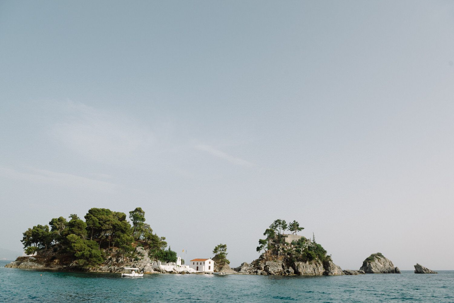 Small rocky islands with vegetation rising from crystal clear Mediterranean waters under blue sky.