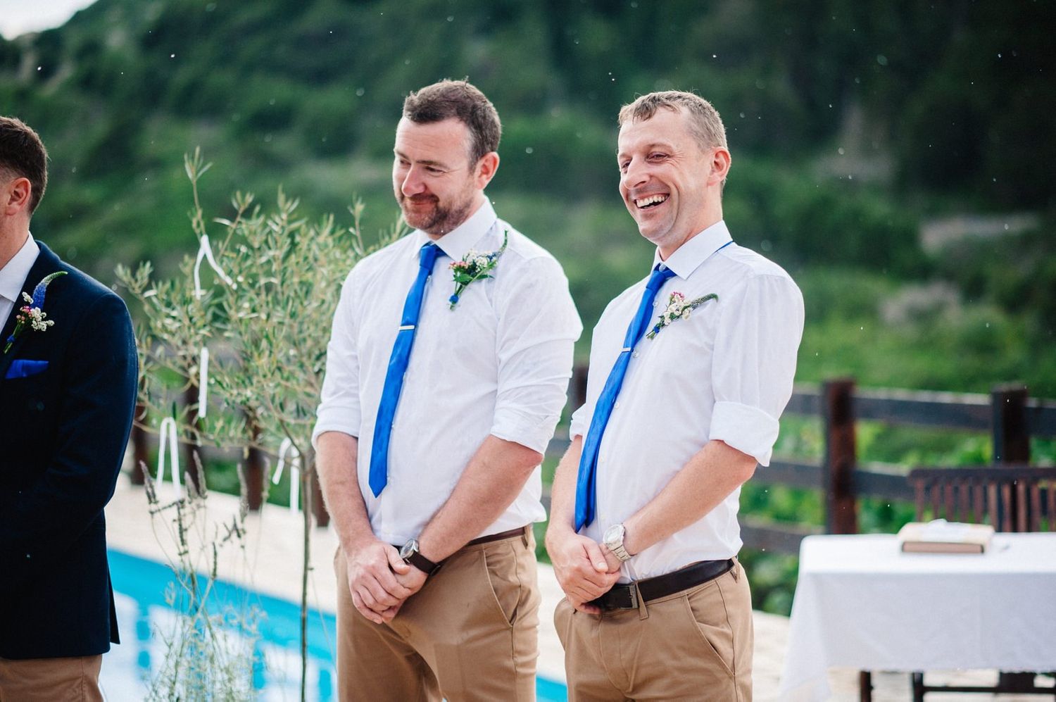 Groomsmen share a lighthearted moment during outdoor poolside wedding ceremony.