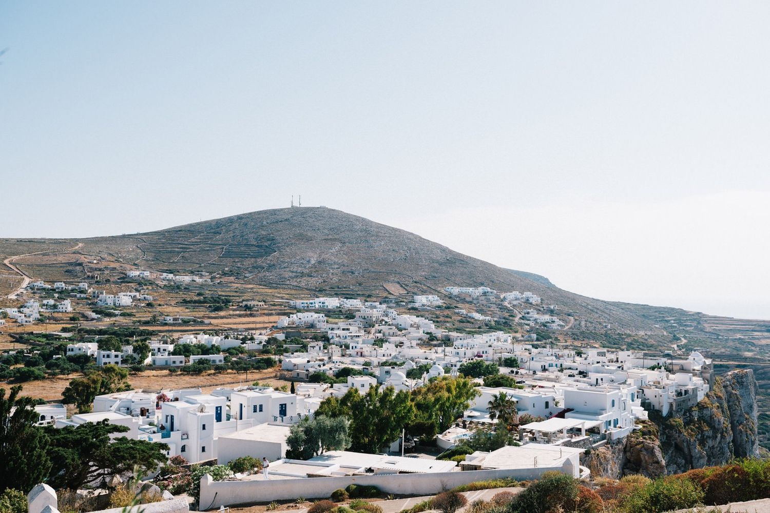 Panoramic view of white village houses nestled in Greek hillside under blue sky.