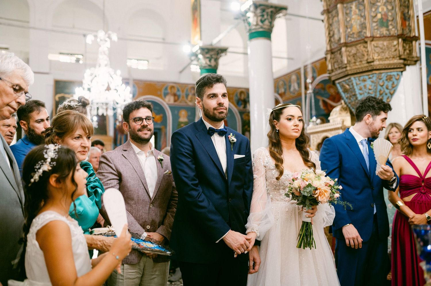 Wedding ceremony scene in ornate church interior with chandelier and decorative columns.