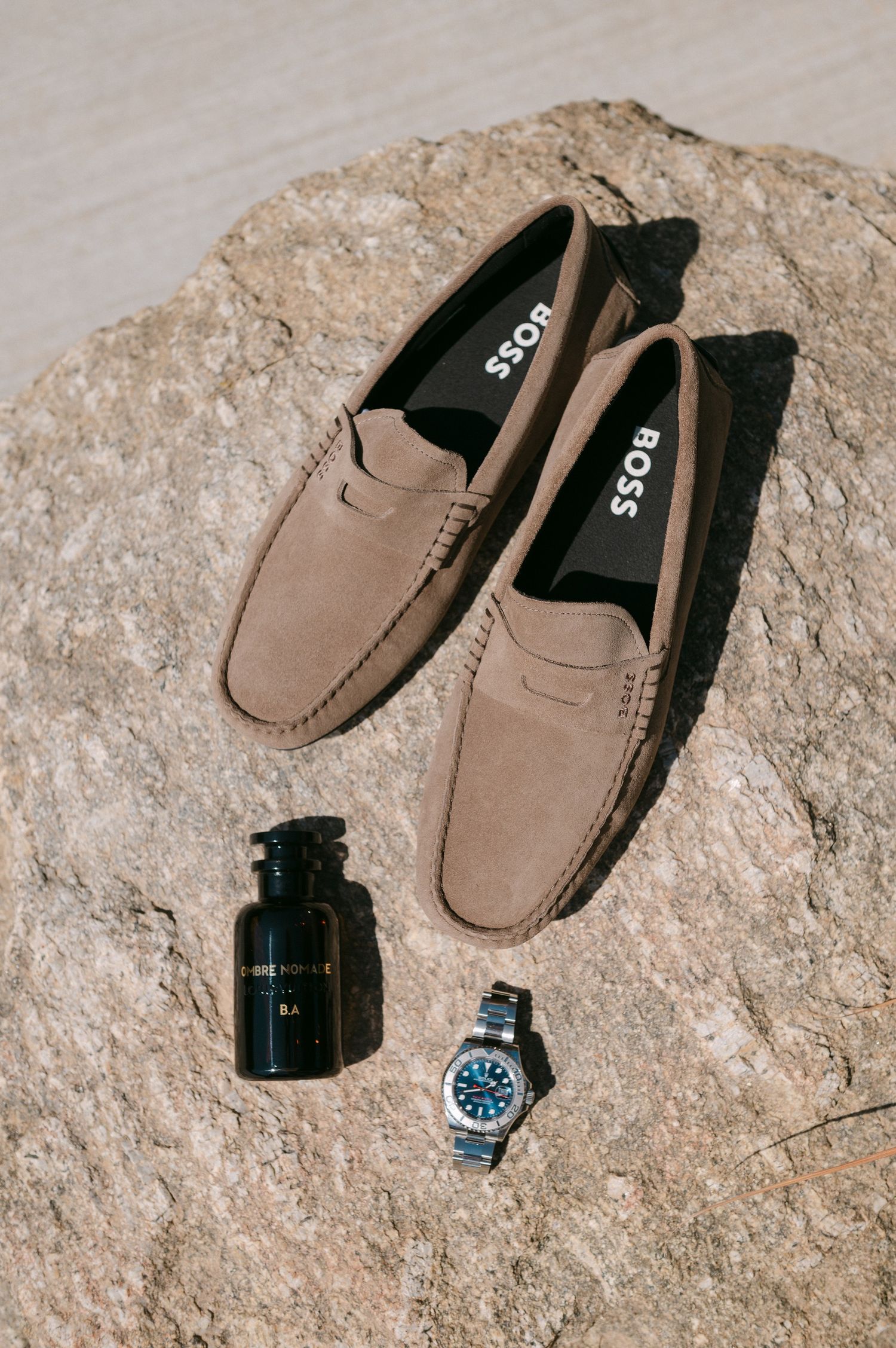 Beige suede loafers and a black watch displayed on textured stone surface in multiple artistic angles.