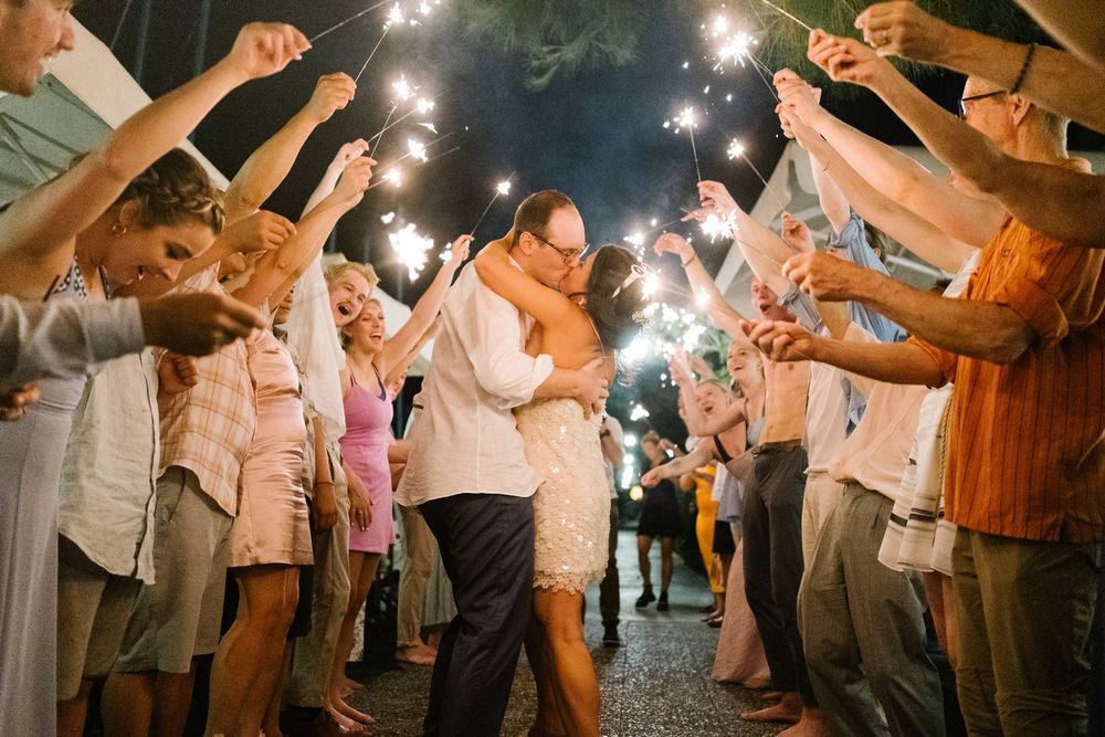 Newlywed couple shares a romantic dance under sparklers held by wedding guests during evening celebration.