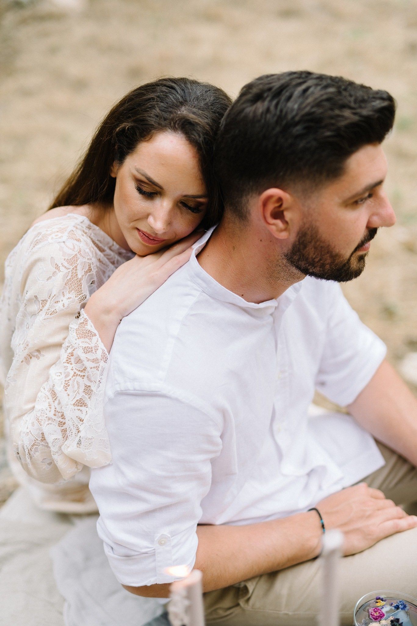 Intimate moment between couple in white clothing sitting together outdoors.