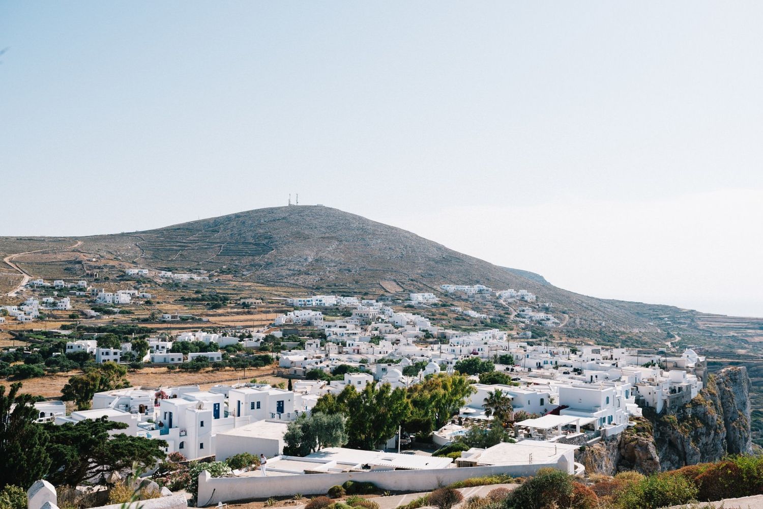 Traditional white Greek village houses scattered across rolling hills under clear blue skies.