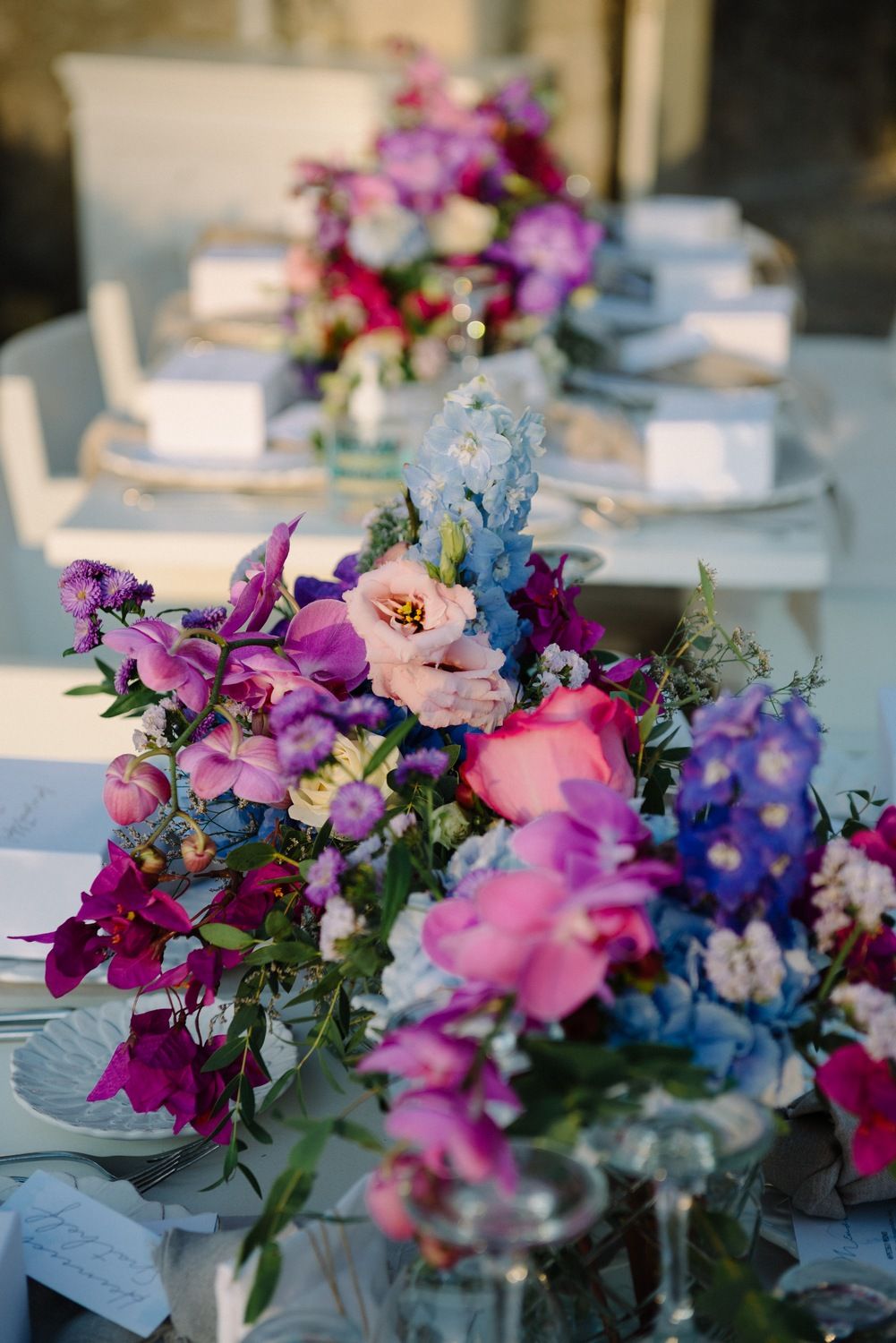 Luxurious table setting with vibrant purple and pink floral arrangements and white place settings.
