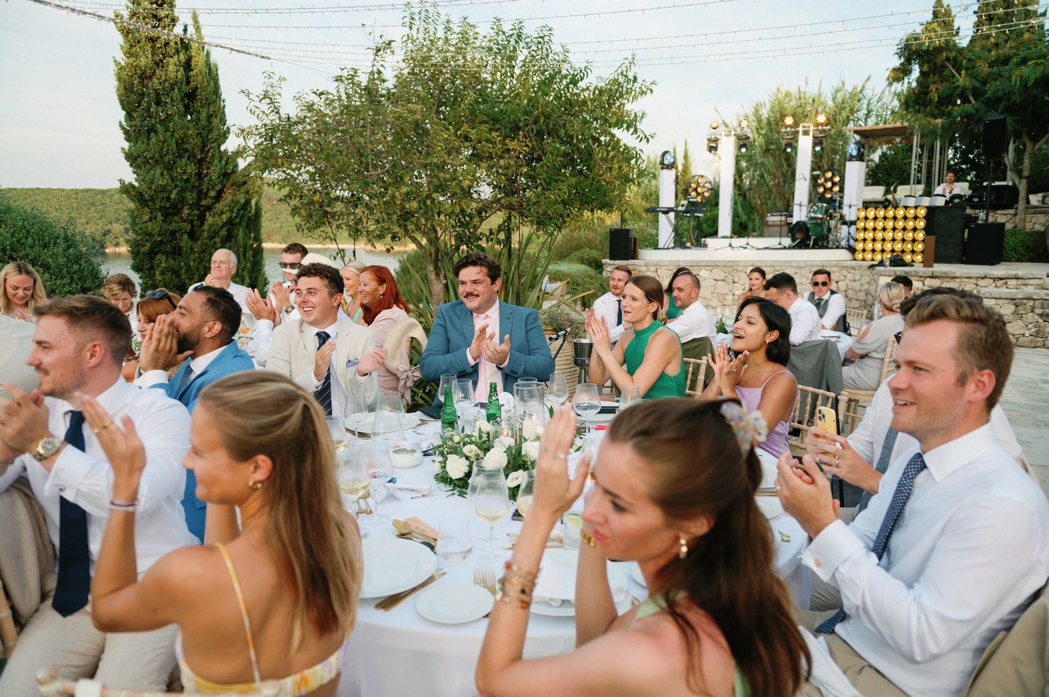 Wedding guests enjoying dinner and conversation at long tables during an outdoor summer reception.