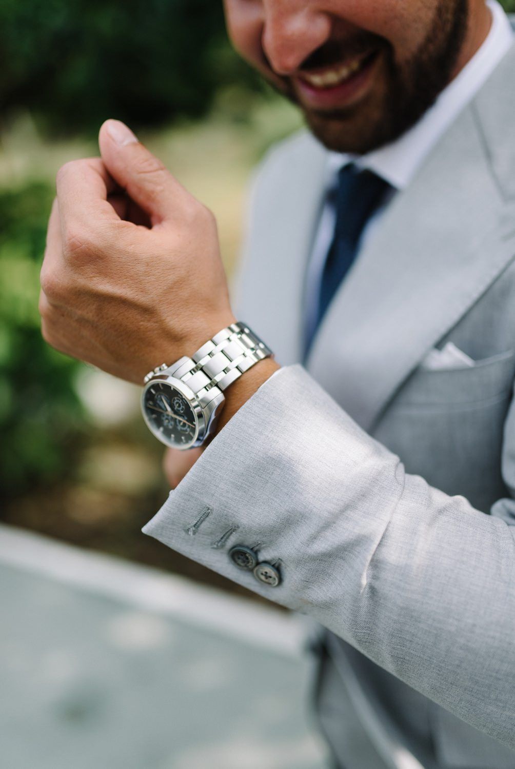 Close-up of silver watch and light gray suit sleeve with cufflink detail.