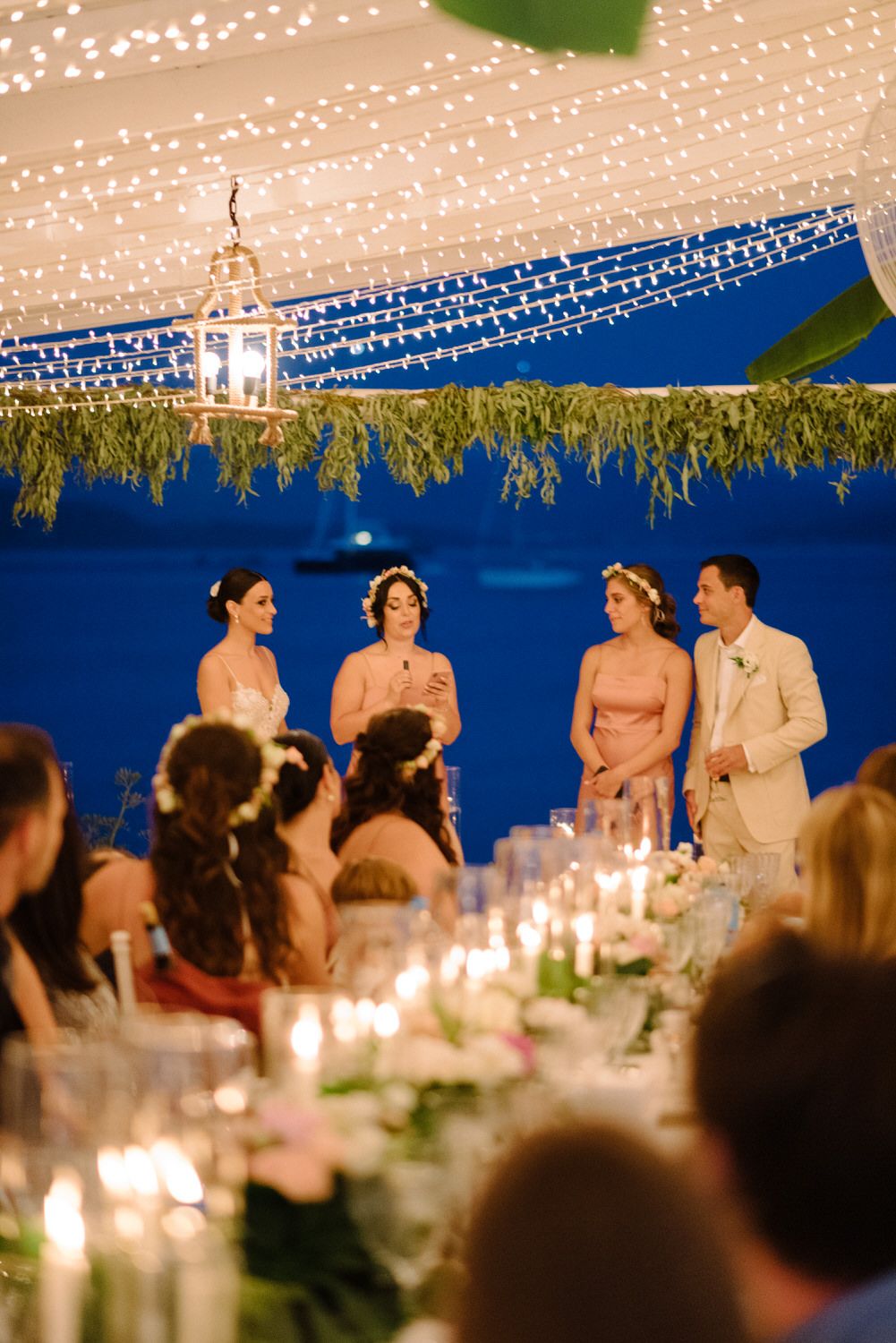 Wedding party stands under a canopy of twinkling lights during an evening outdoor reception celebration.