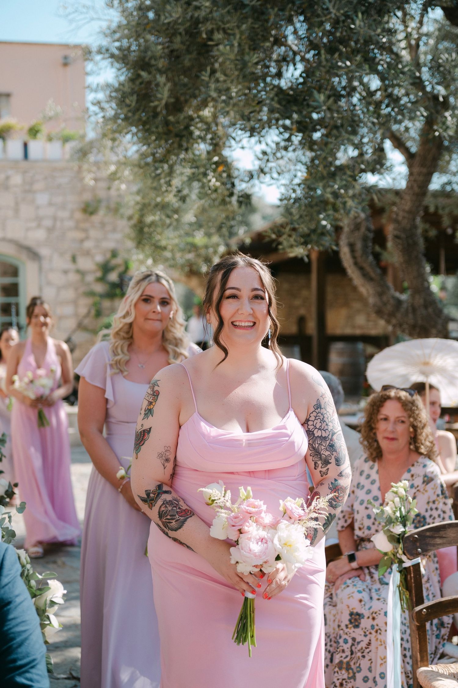 Bridesmaids in pink and lavender dresses share candid moments during an outdoor wedding celebration.