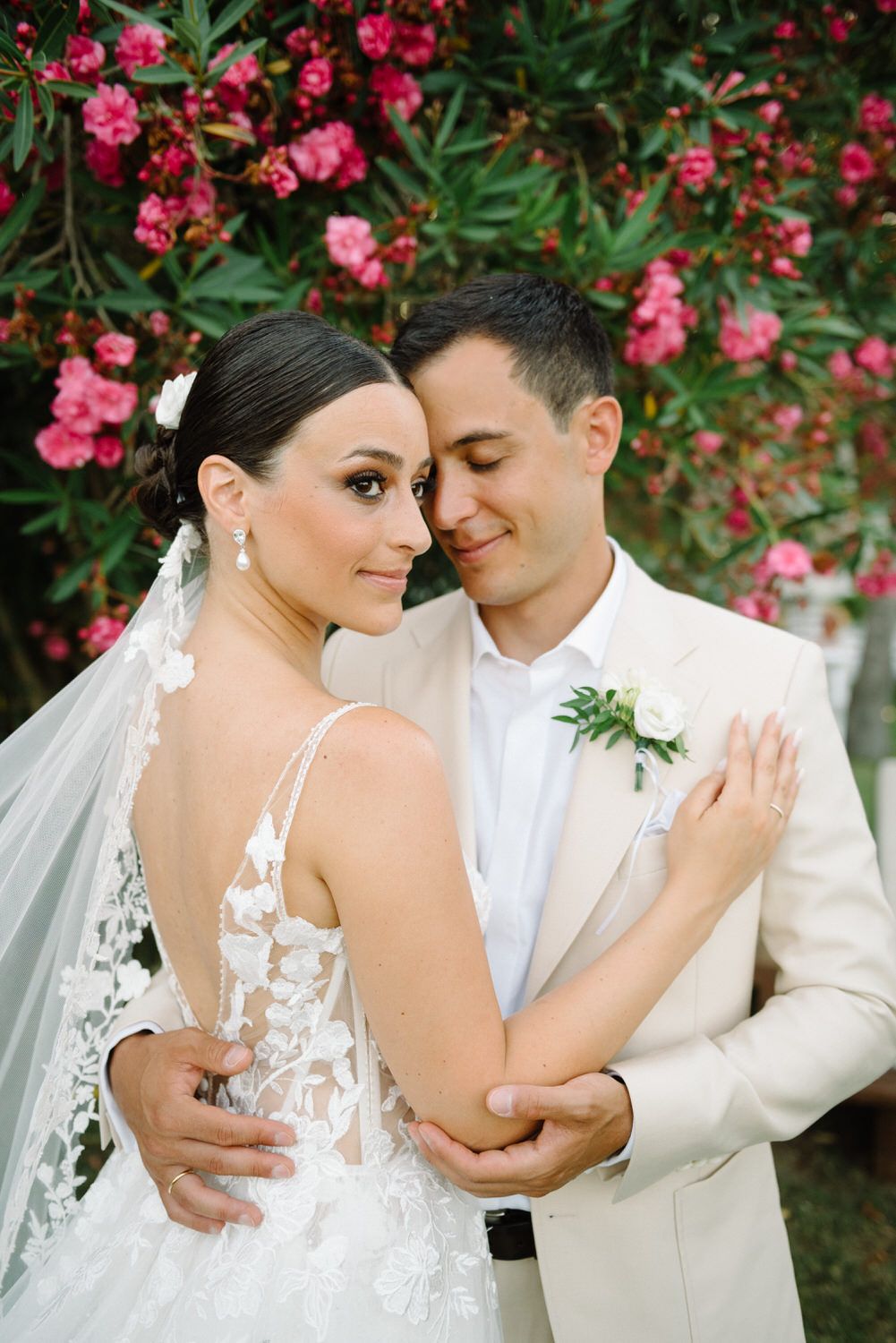Wedding couple embracing near pink bougainvillea flowers in garden setting.