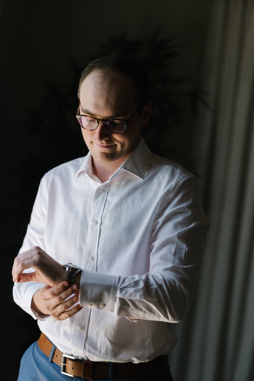 A person in a white dress shirt and glasses looking down at their watch.