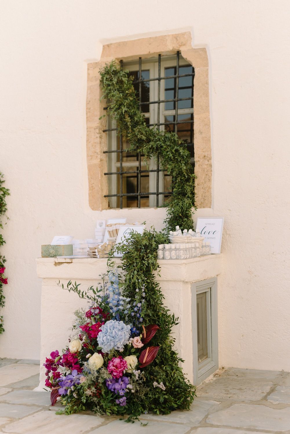 Romantic floral display with cascading greenery around window and colorful blooms on stone ledge.