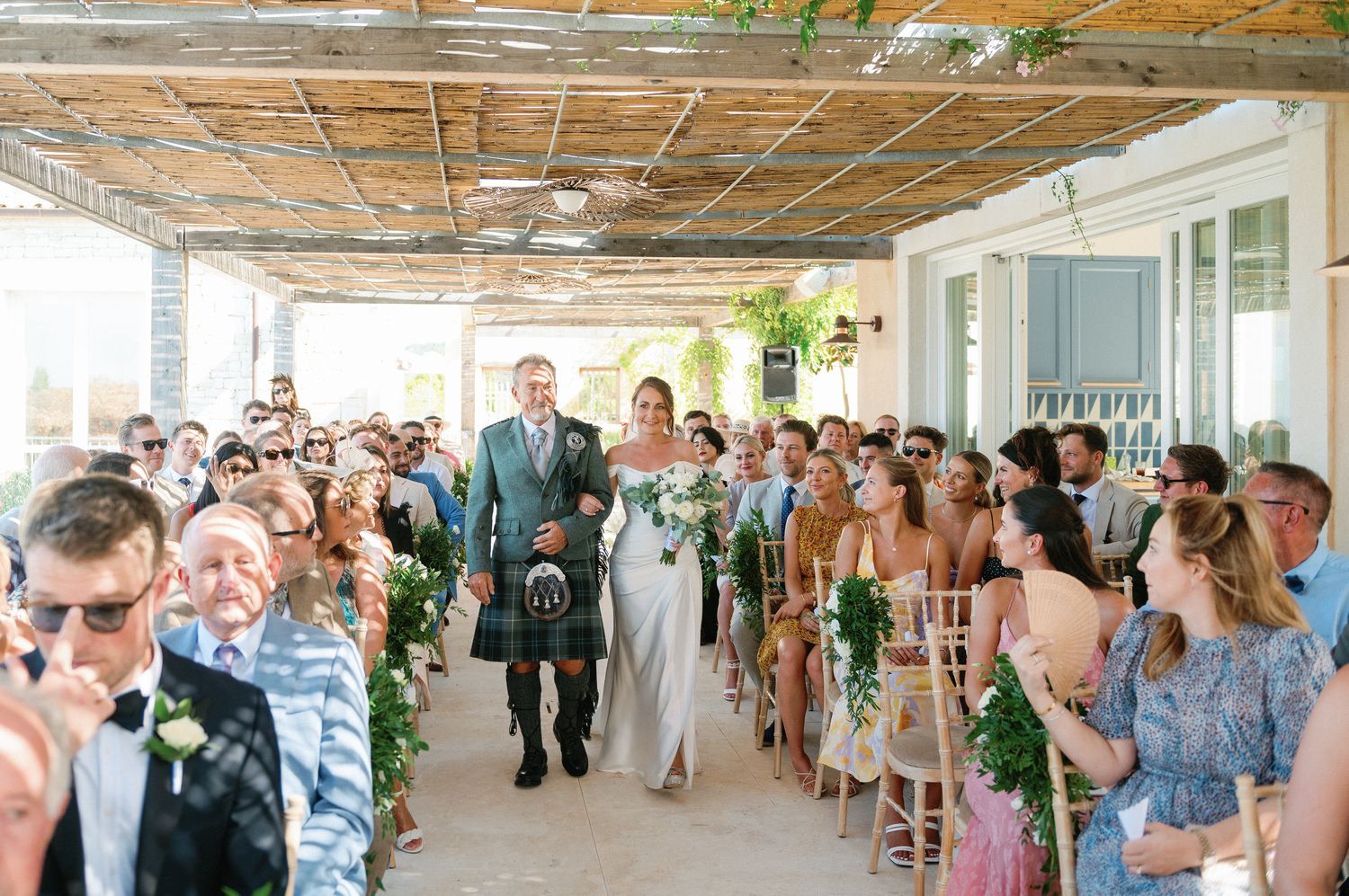 Outdoor wedding ceremony with guests lining bamboo-covered walkway.