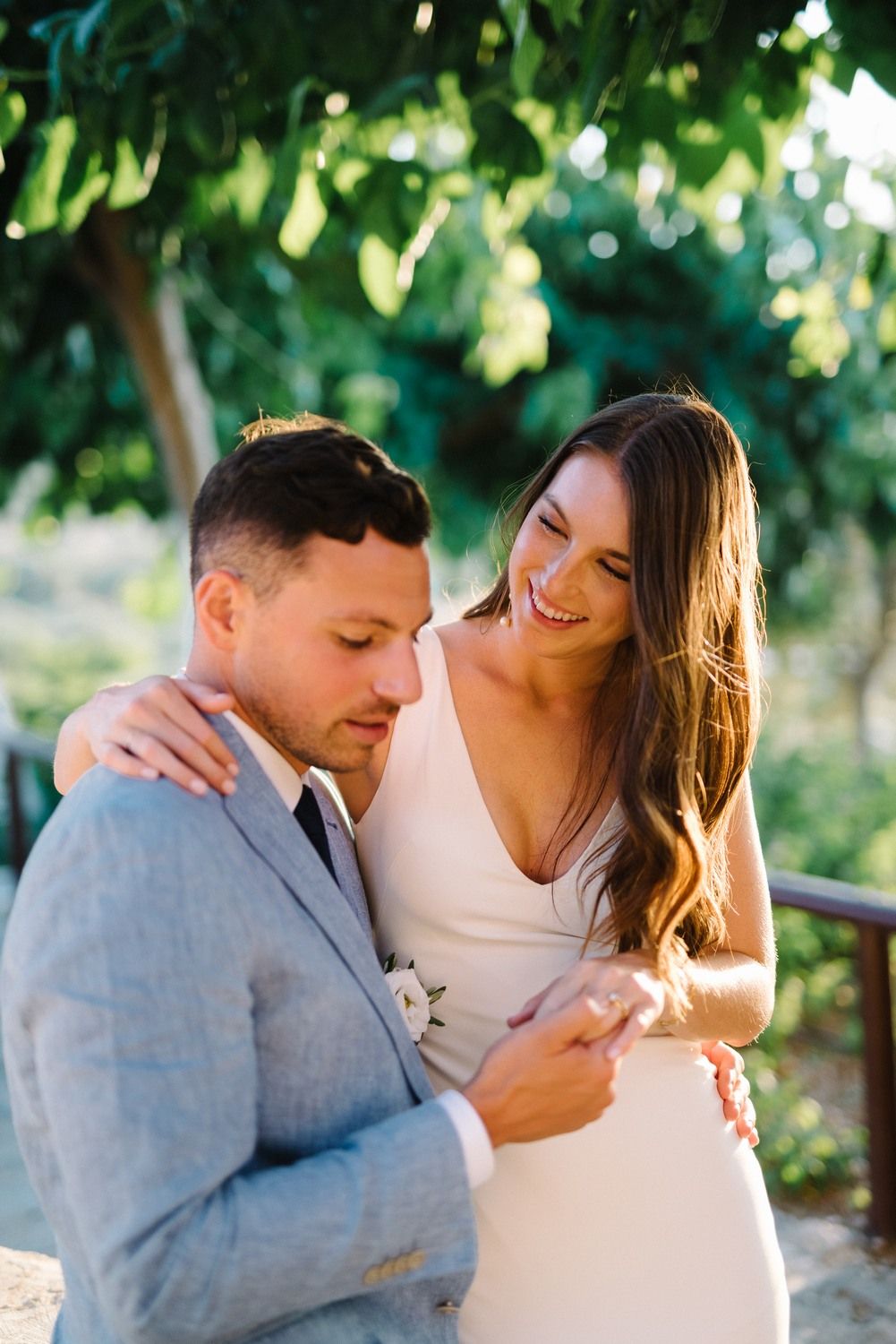 A tender moment between newlyweds in formal attire against a sunlit garden backdrop.