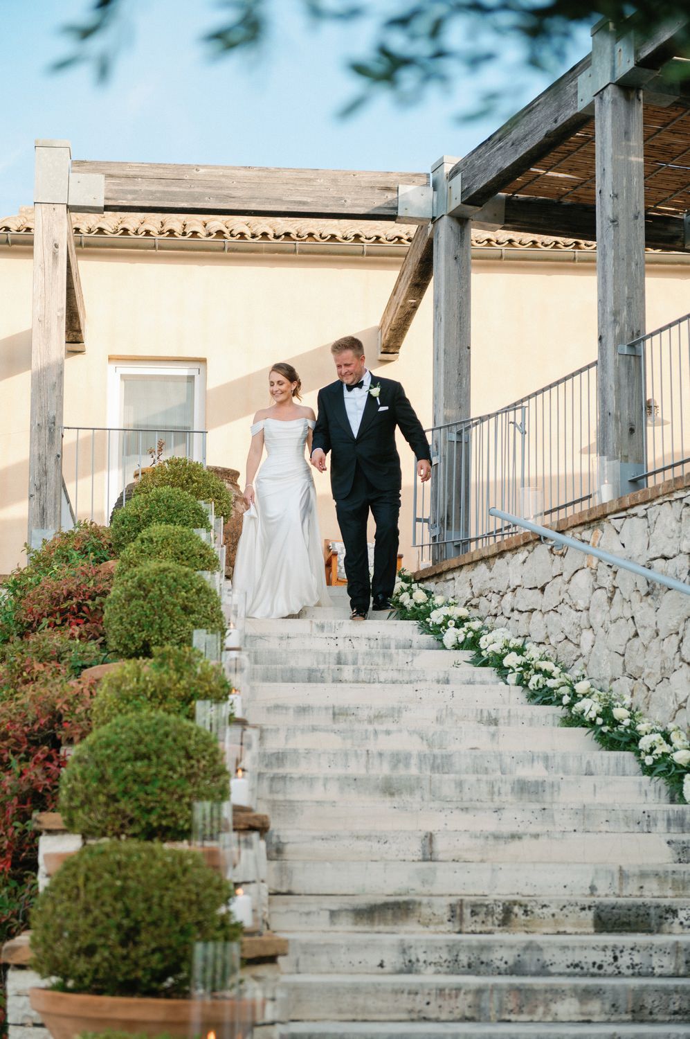 Couple descending elegant stone steps adorned with greenery at a wedding venue.