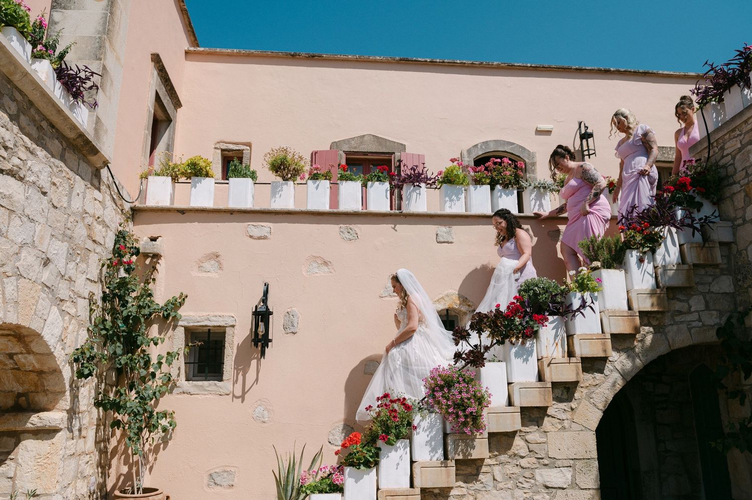 Mediterranean style staircase decorated with potted flowers and plants along pink walls against bright blue sky.