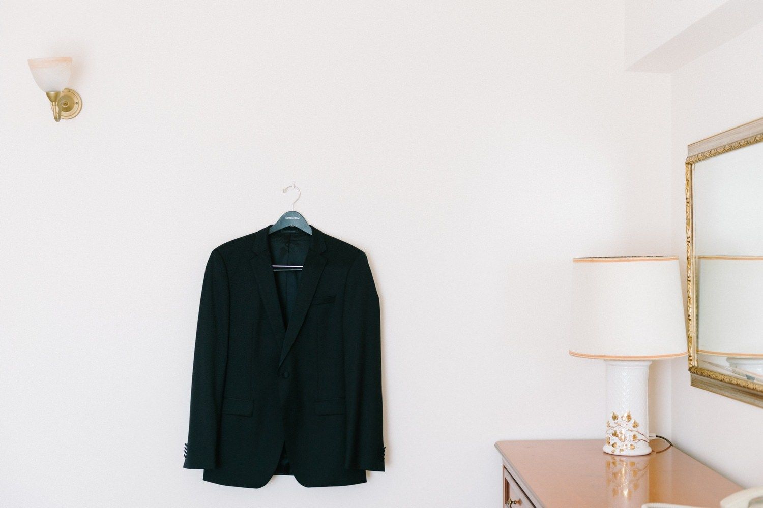 Black suit jacket hanging on white wall with minimal decor.