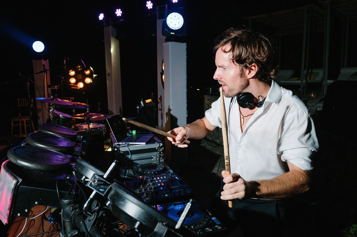 DJ focused on mixing at turntables with purple stage lighting in background.