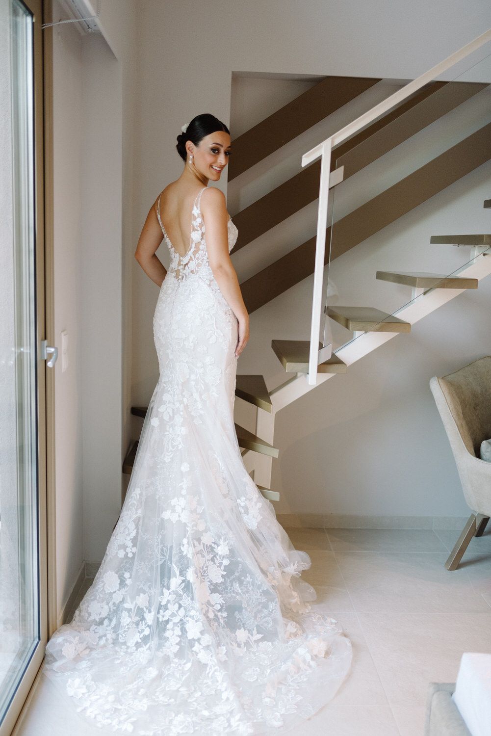 A stunning lace mermaid wedding gown with intricate floral details and a flowing train photographed near modern stairs.