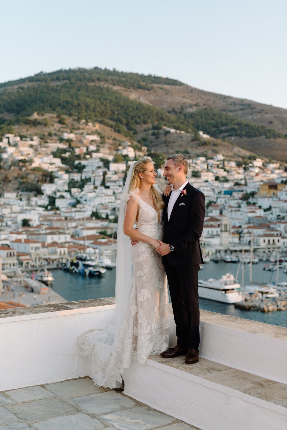 Newlyweds share intimate moment on balcony overlooking Mediterranean harbor town.
