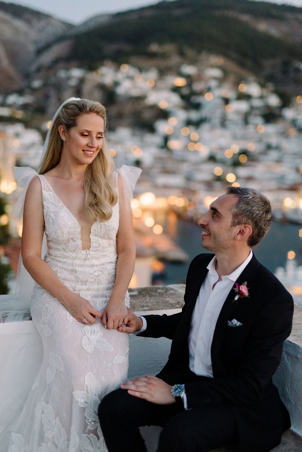Couple shares intimate moment on white terrace overlooking harbor town at twilight.