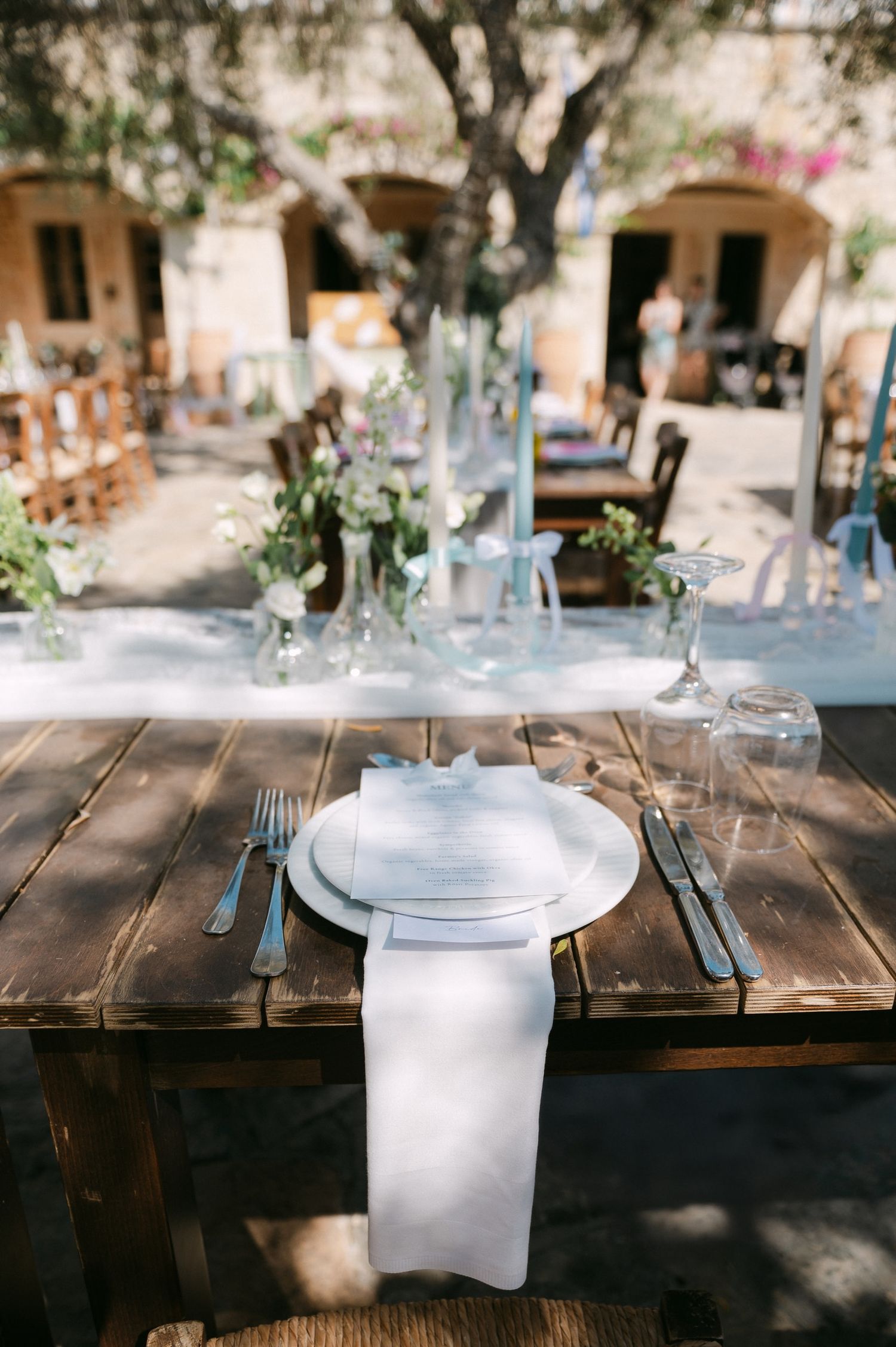 Rustic outdoor table setting with white plates and napkins under dappled sunlight at a garden venue.