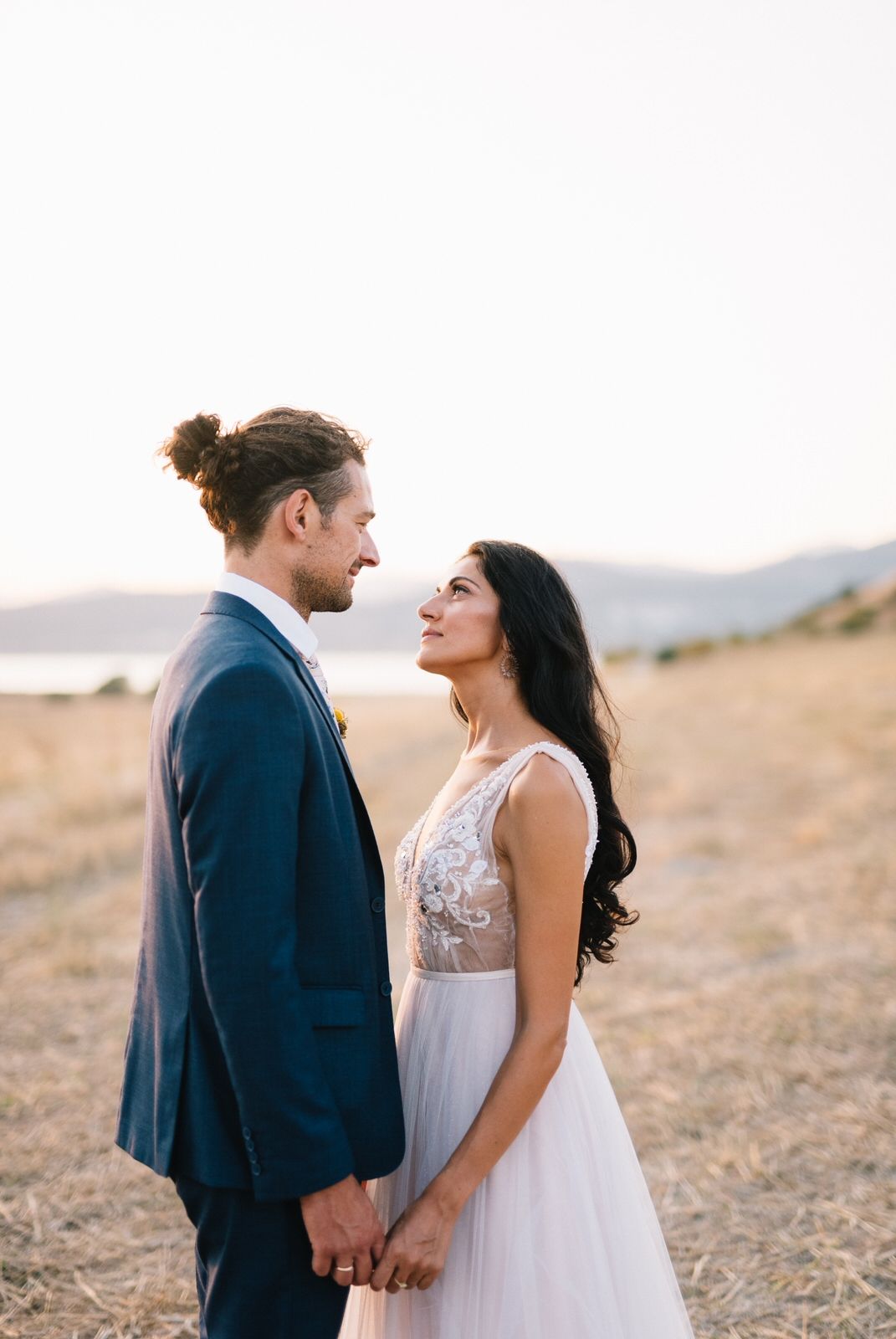 Couple in wedding attire gazes at each other against mountain backdrop.