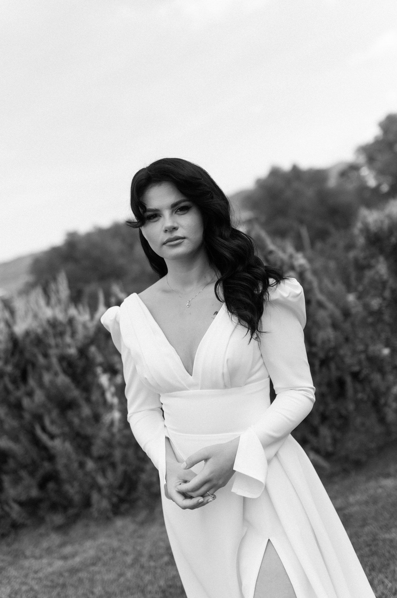 Black and white portrait of bride in a white dress posing against a blurred natural outdoor background.