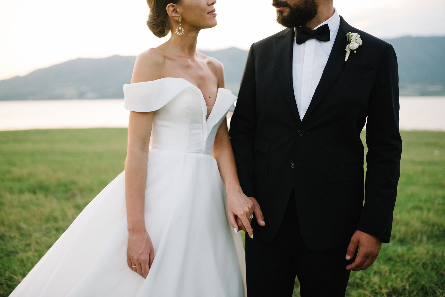 A romantic wedding couple embraces outdoors against a scenic mountain lake backdrop during their special day.