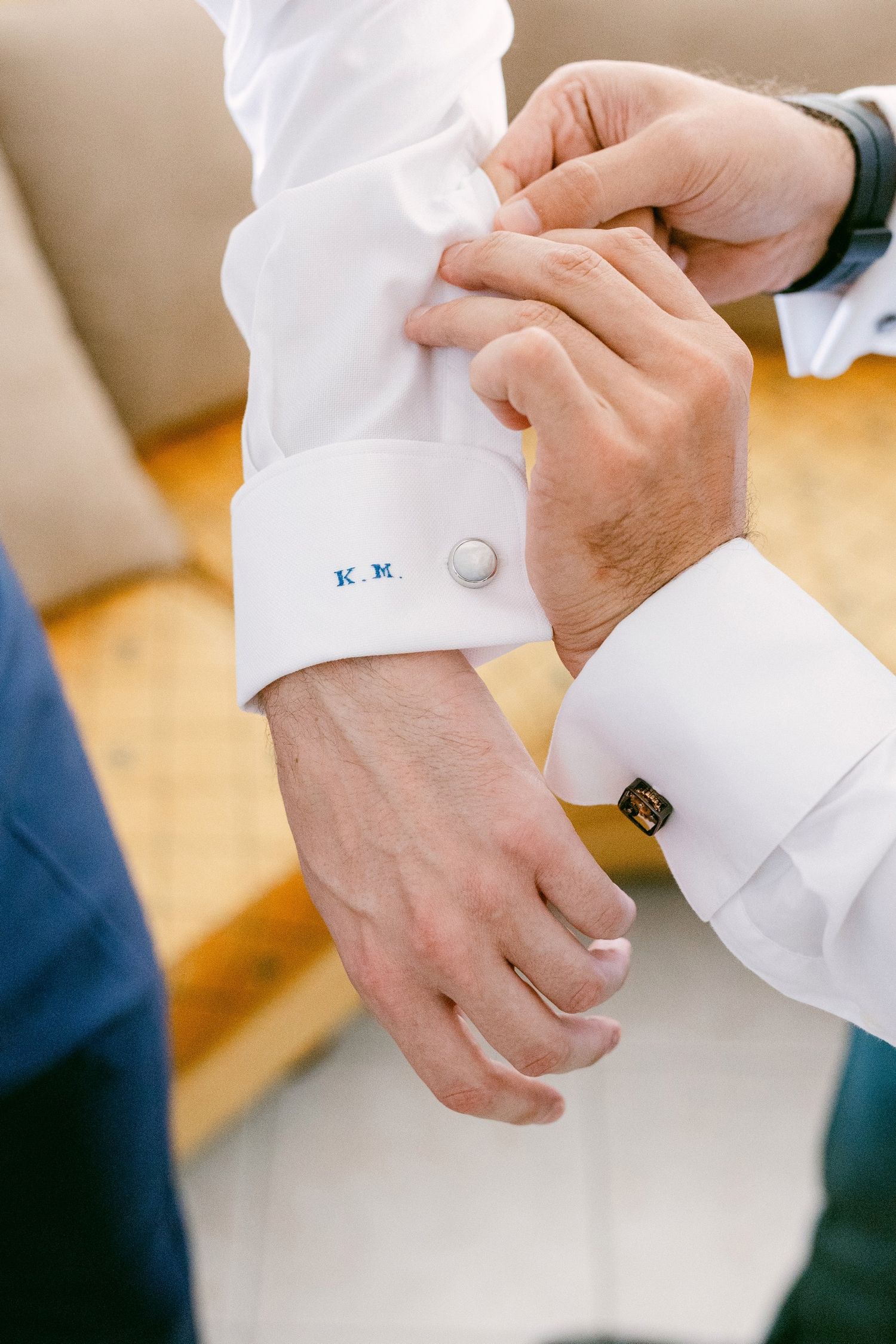 Close-up of hands adjusting white dress shirt cuff with monogrammed initials on formal attire.