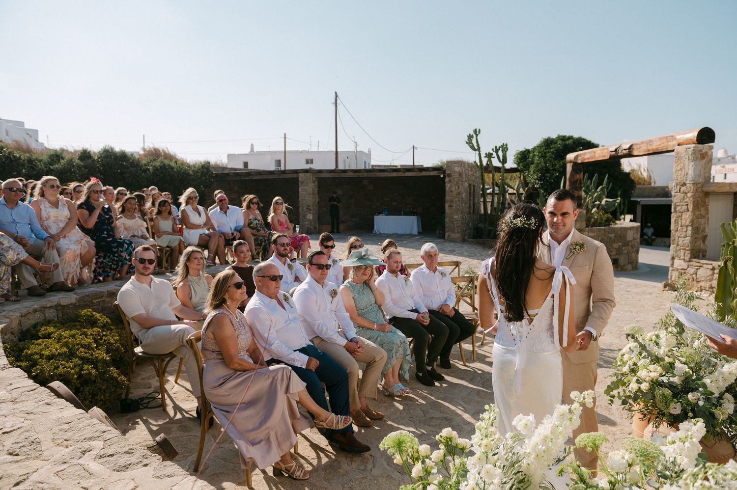 Guests celebrate at an outdoor beach wedding ceremony with white floral arrangements and ocean views.