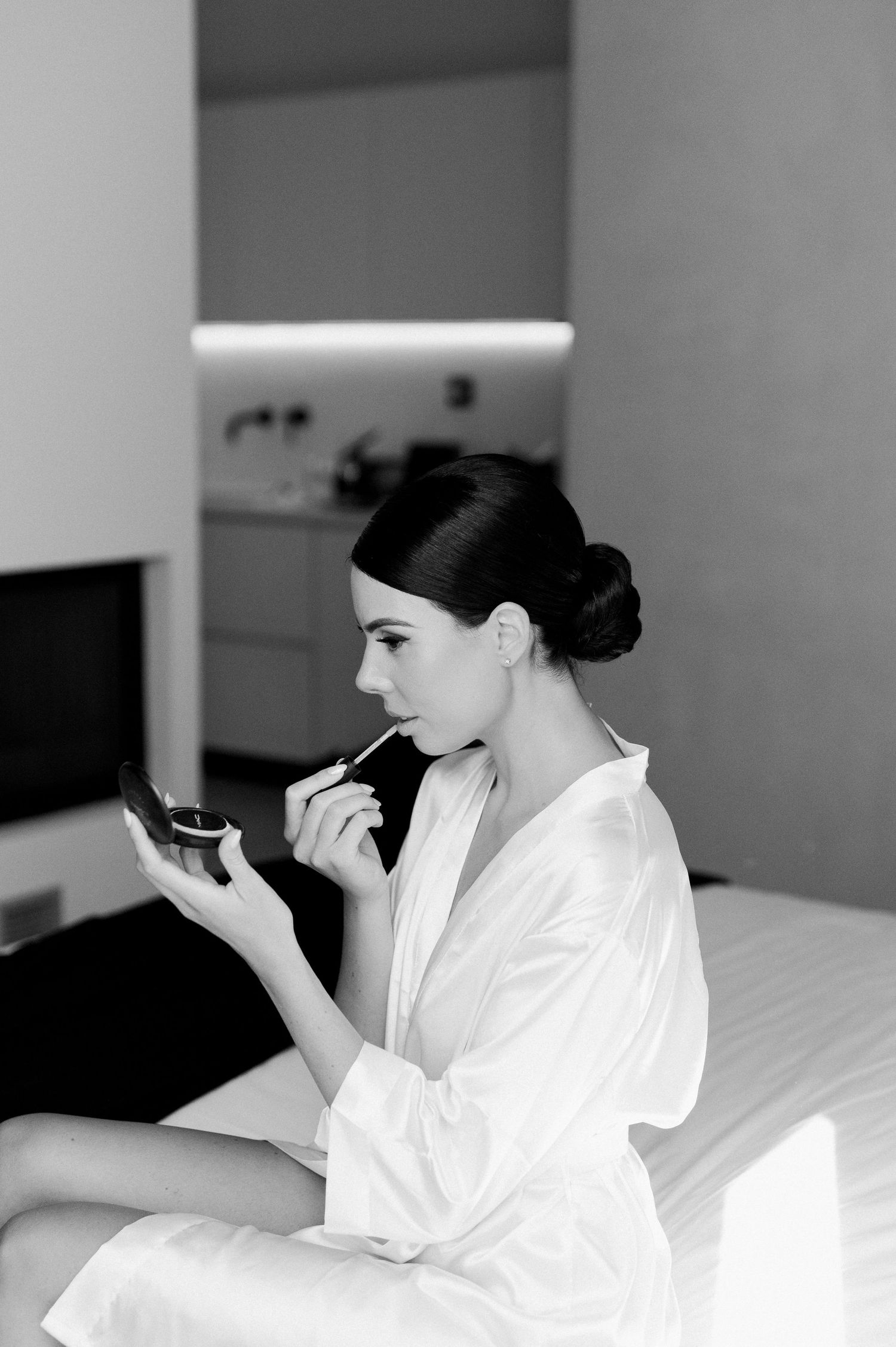 A person in white robe lies on a bed while applying makeup in a series of black and white photographs.