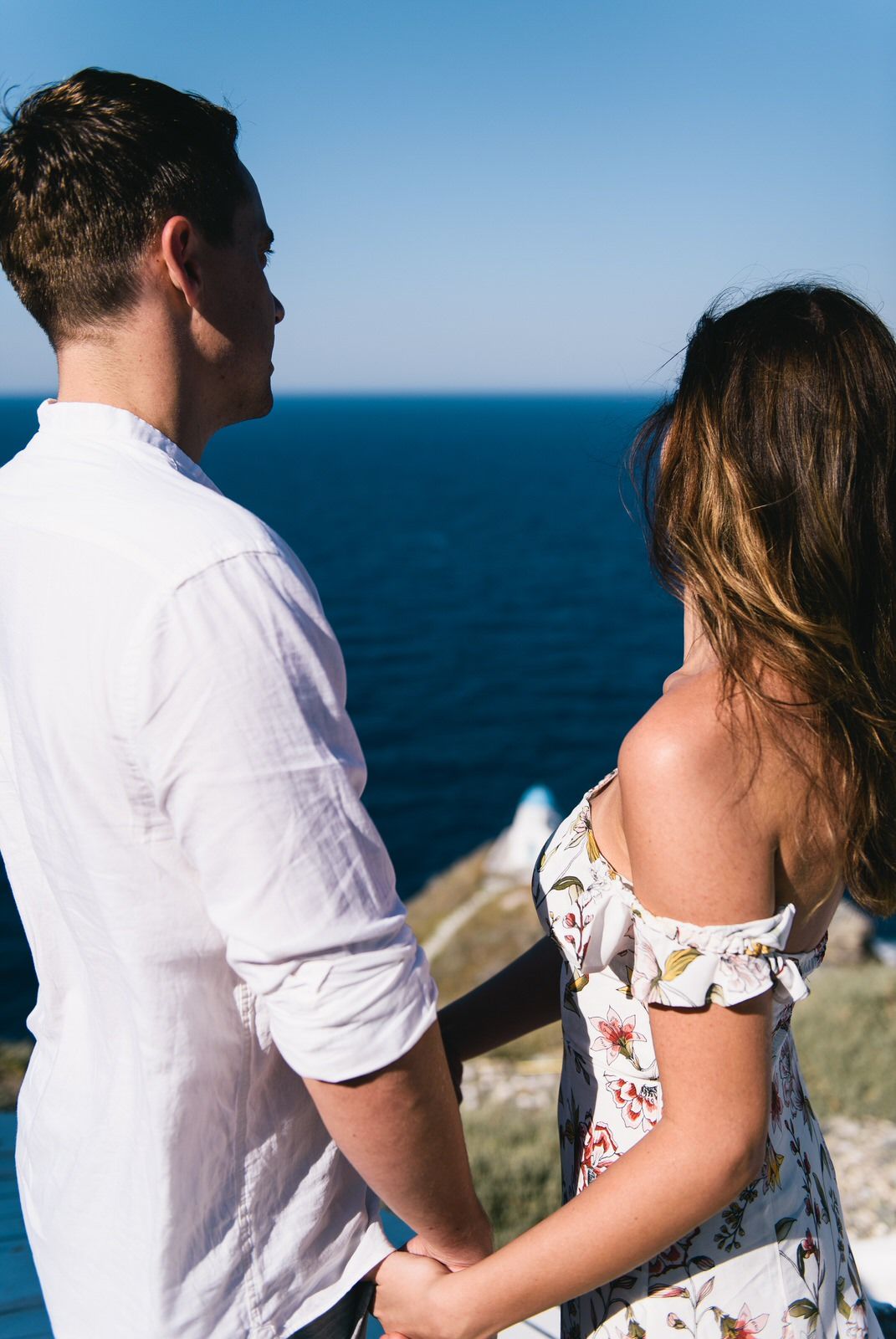 Couple sharing an intimate moment overlooking the deep blue Mediterranean Sea against a clear sky backdrop.