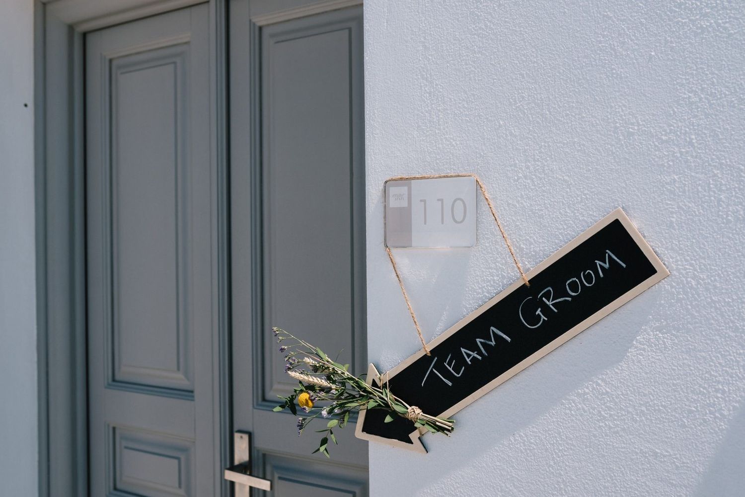 A gray door with a small decorative chalkboard sign and flowers mounted on it.