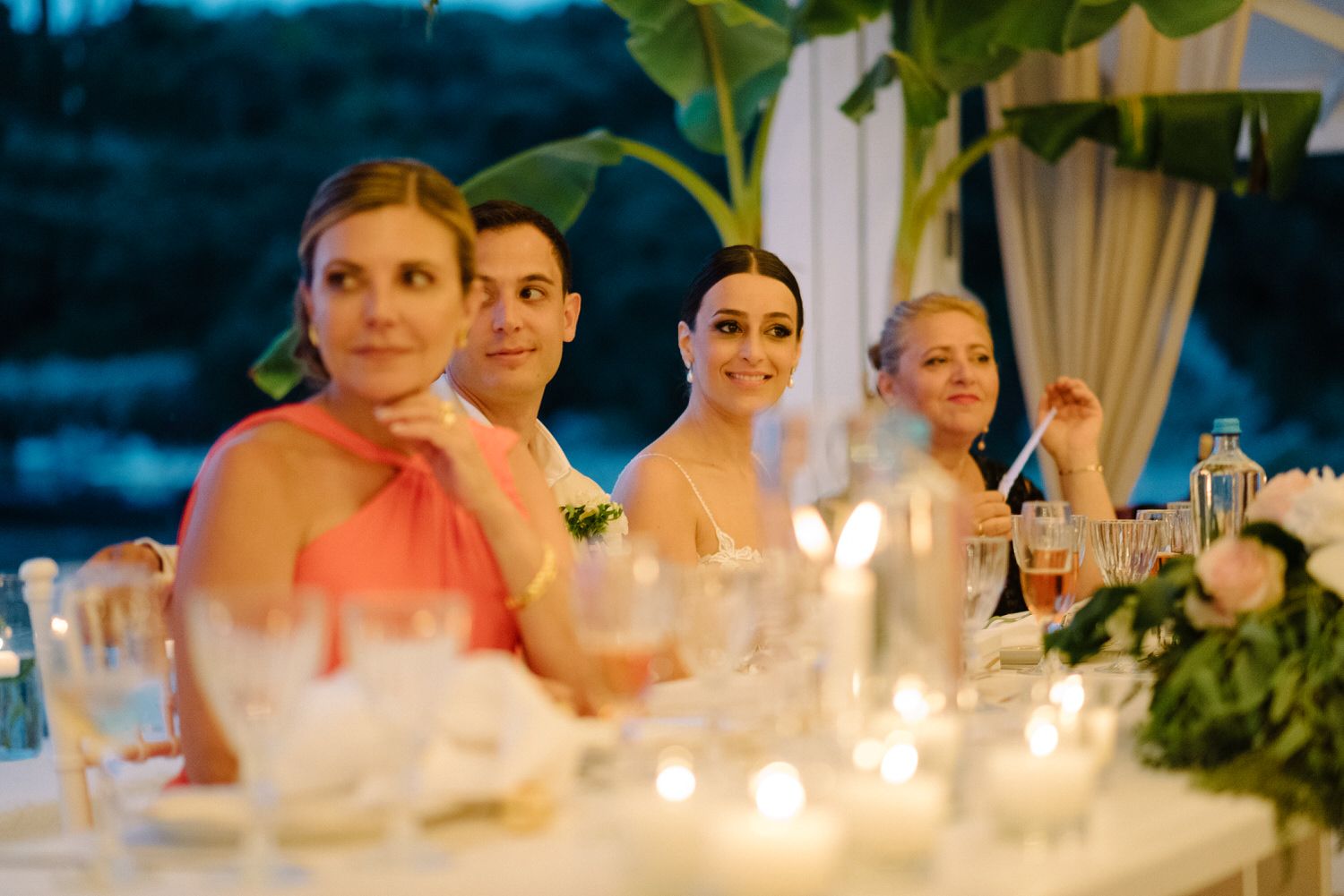 Candlelit dinner celebration at sunset with guests seated at an elegant table under white drapery.
