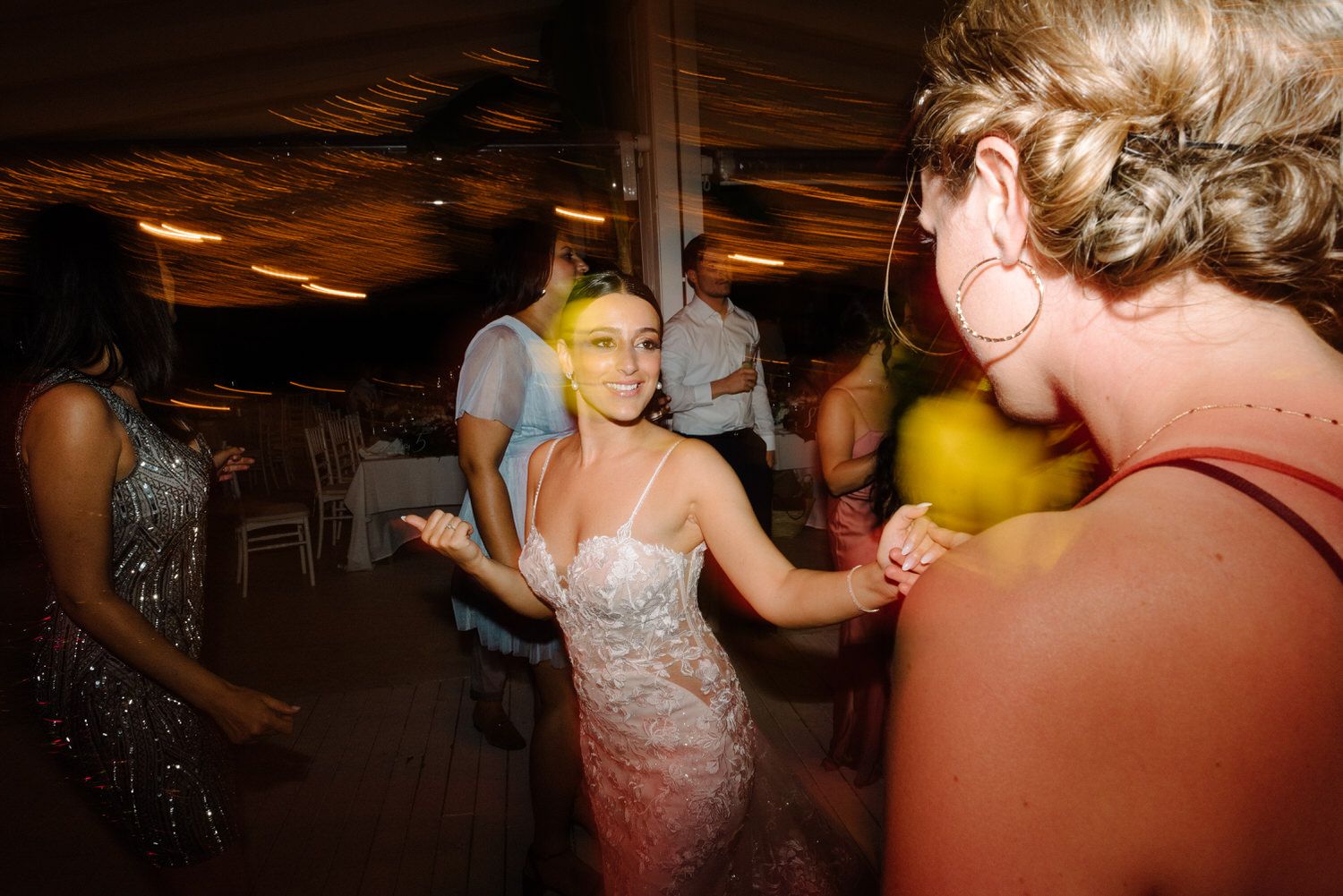 Guests dance and celebrate at an indoor wedding reception with ambient lighting.
