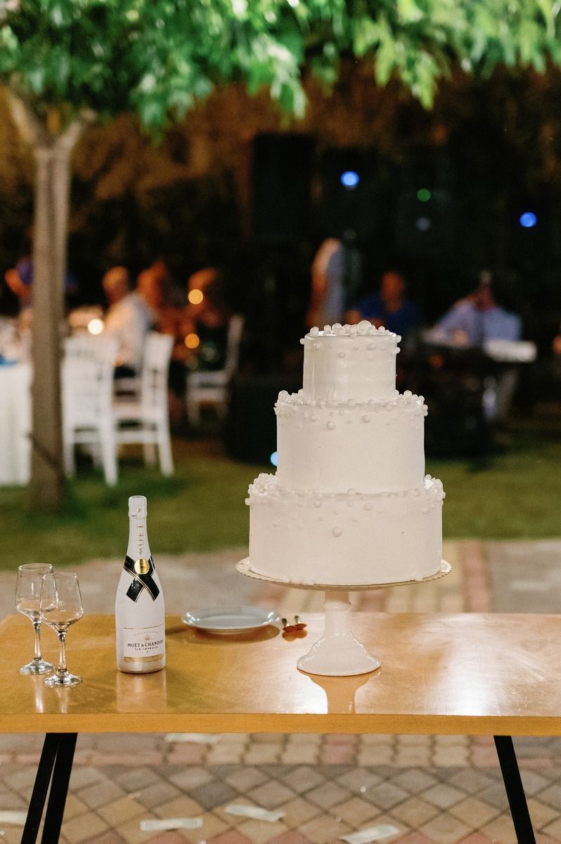 Elegant three-tiered white wedding cake displayed on wooden table with champagne bottle.