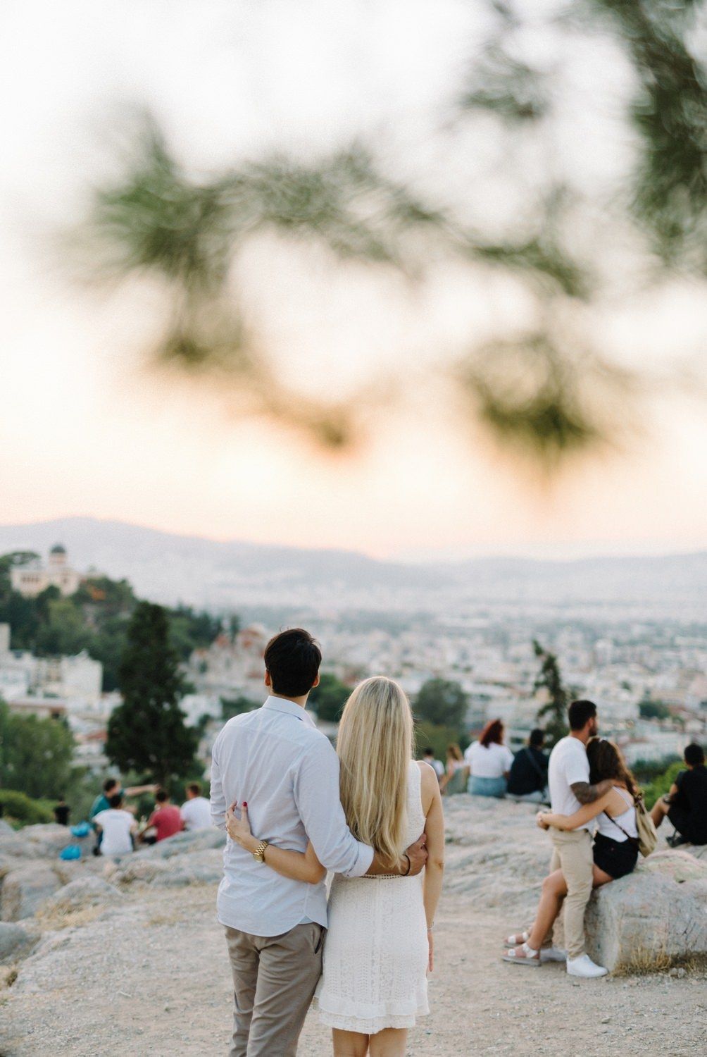Couple overlooking Athens cityscape at sunset from a hilltop viewpoint.