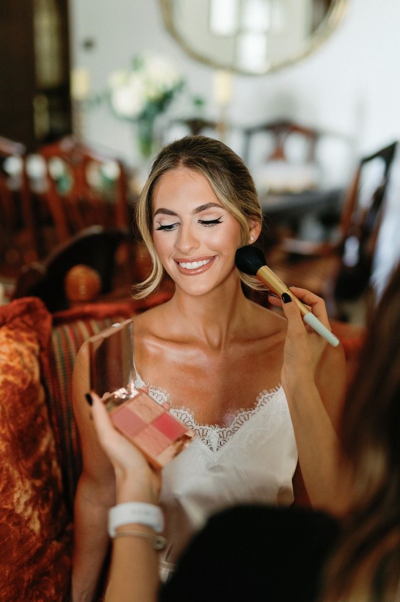 Someone having makeup applied while holding a cosmetic palette during wedding preparations.