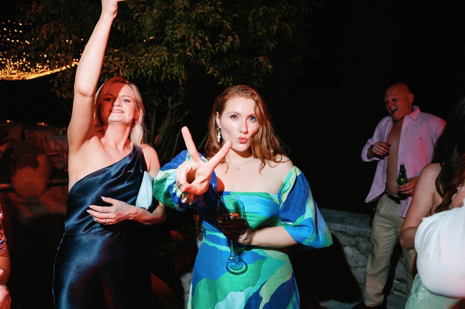 Party guests in formal attire dancing under outdoor lighting at evening event.