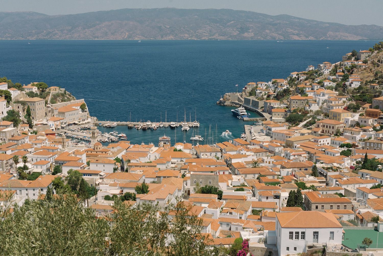 Aerial view of Mediterranean coastal town with terracotta roofs and boats in harbor.
