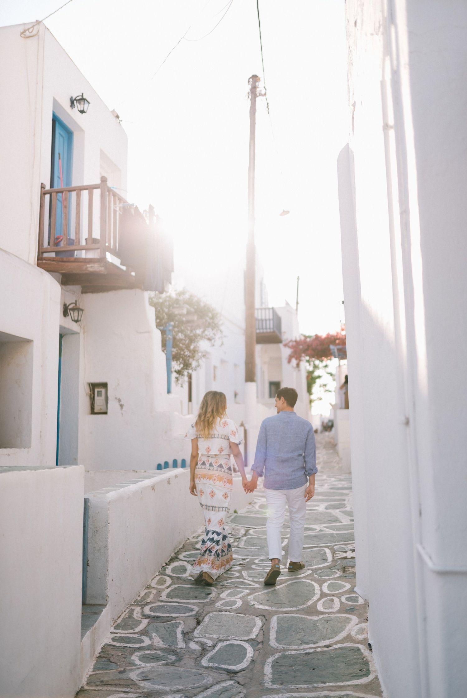 A couple walks hand in hand down a picturesque cobblestone street in Santorini.