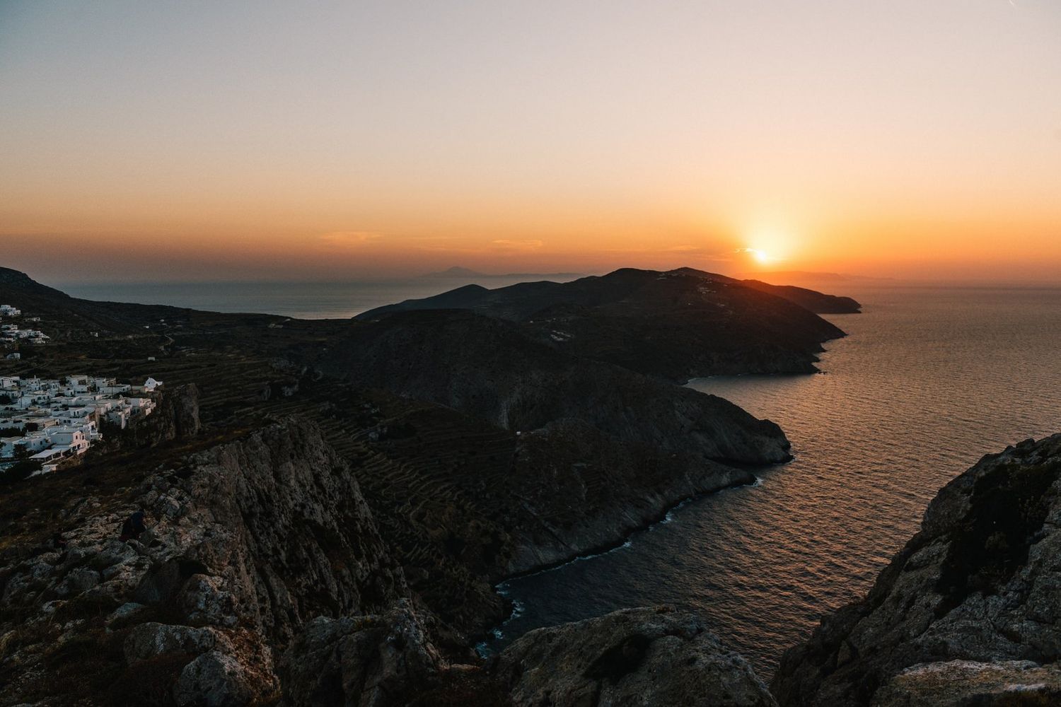 Dramatic sunset over a coastal mountain landscape with deep blue waters and rocky cliffs.