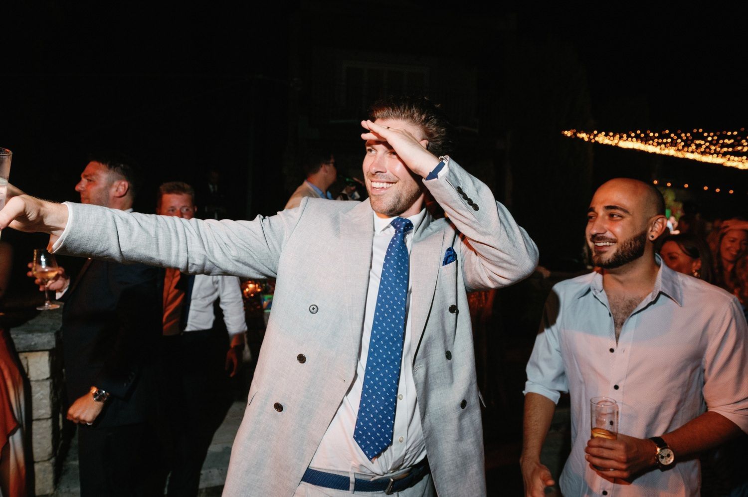 Dancing wedding guests celebrating outdoors under string lights at night.