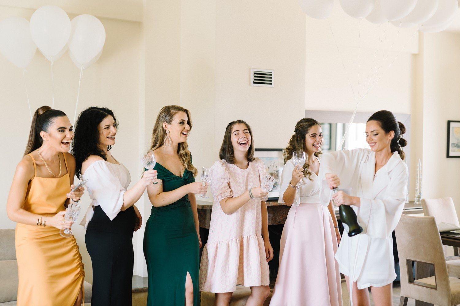 Wedding party celebrating with champagne in coordinated dresses of yellow, green, and pink.