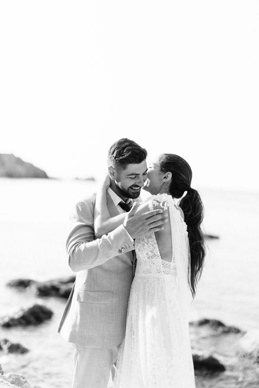 Black and white photo of newlyweds sharing an intimate moment on a rocky beach.