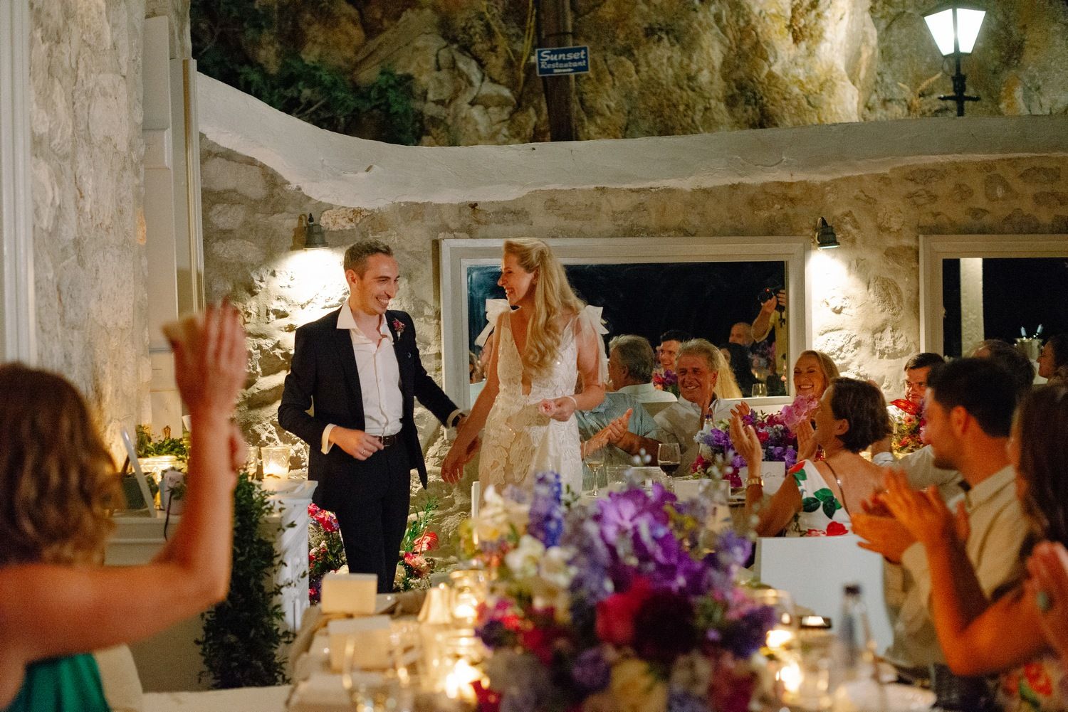 Wedding reception dinner celebration in an elegant stone venue with floral decorations.